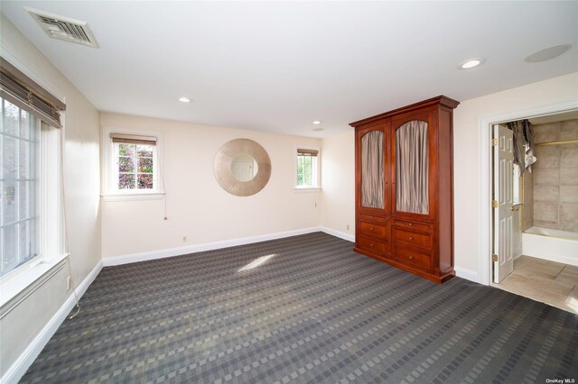 empty room featuring visible vents, dark carpet, and baseboards