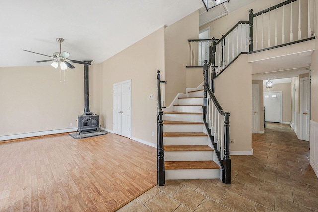 staircase with a baseboard radiator, a high ceiling, wood finished floors, a ceiling fan, and a wood stove