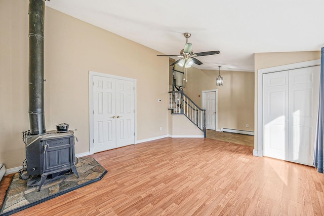 unfurnished living room with light wood finished floors, a baseboard radiator, a wood stove, stairs, and vaulted ceiling