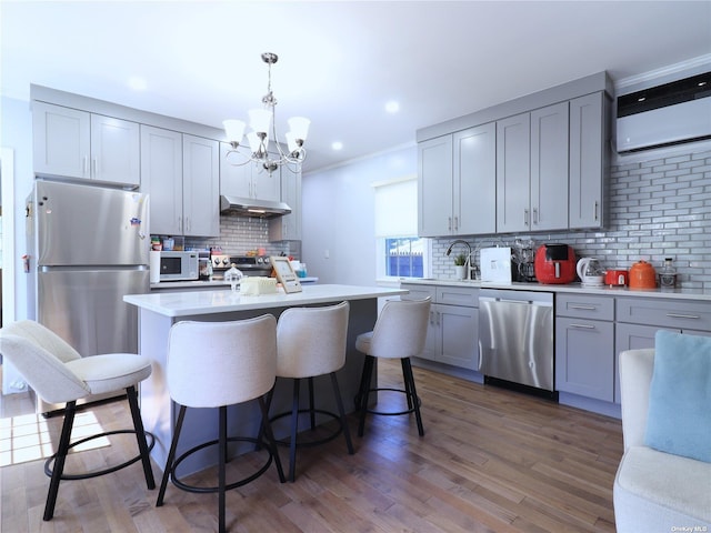 kitchen featuring stainless steel appliances, gray cabinets, light countertops, wood finished floors, and under cabinet range hood