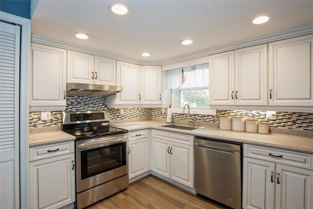 kitchen with appliances with stainless steel finishes, white cabinets, a sink, wood finished floors, and under cabinet range hood