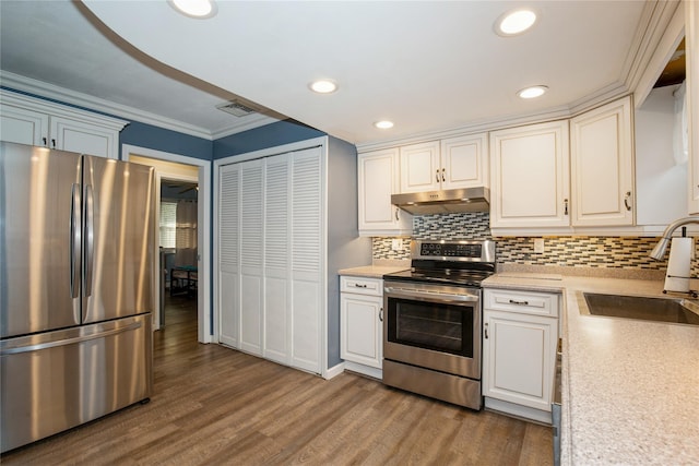 kitchen with appliances with stainless steel finishes, wood finished floors, light countertops, under cabinet range hood, and a sink