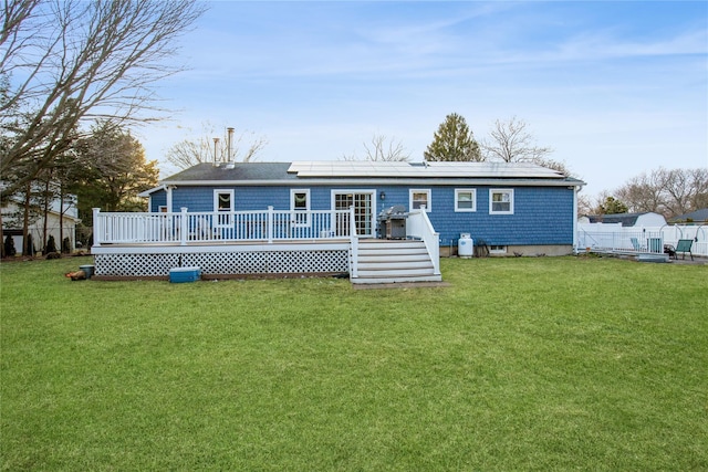 rear view of property with a yard, fence, a wooden deck, and solar panels