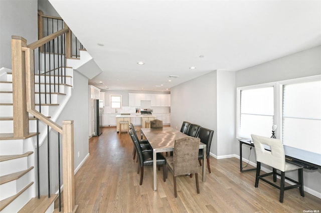 dining room with light wood-style floors, stairway, and baseboards