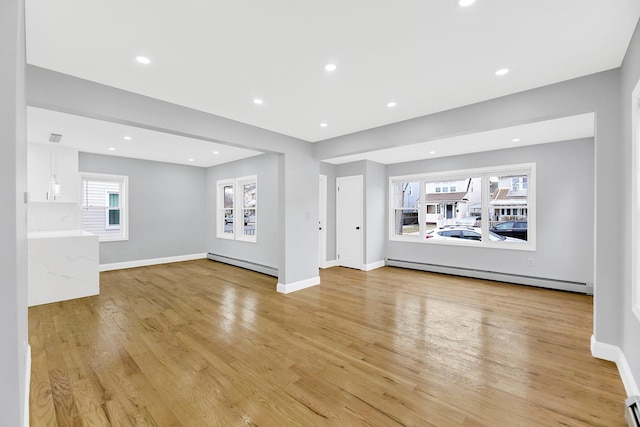 unfurnished living room featuring a baseboard heating unit, baseboard heating, baseboards, and light wood-style floors