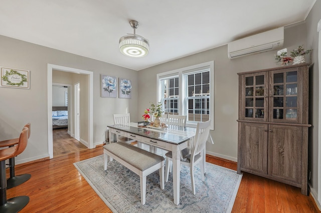 dining area featuring light wood-type flooring, a wall mounted air conditioner, and baseboards