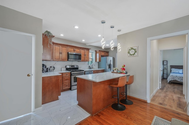 kitchen featuring brown cabinetry, appliances with stainless steel finishes, a kitchen breakfast bar, a peninsula, and marble finish floor