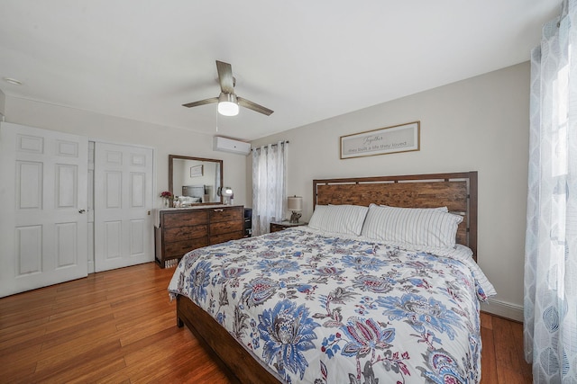 bedroom with a ceiling fan, an AC wall unit, a closet, and wood finished floors