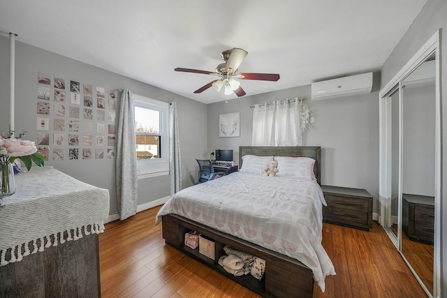 bedroom featuring baseboards, a ceiling fan, a wall unit AC, wood-type flooring, and a closet