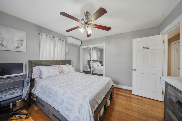 bedroom with wood finished floors, a ceiling fan, baseboards, a closet, and a wall mounted AC