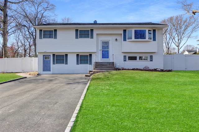 raised ranch with aphalt driveway, a front lawn, fence, and a gate