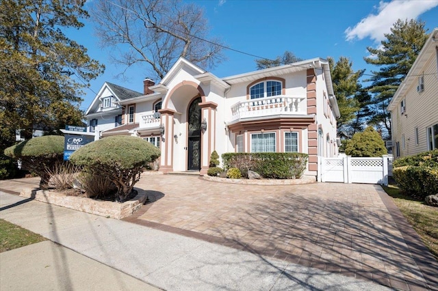 view of front of house featuring decorative driveway, stucco siding, a gate, fence, and a balcony