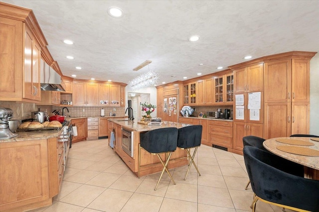 kitchen with a center island with sink, light tile patterned floors, stainless steel microwave, a sink, and a kitchen breakfast bar