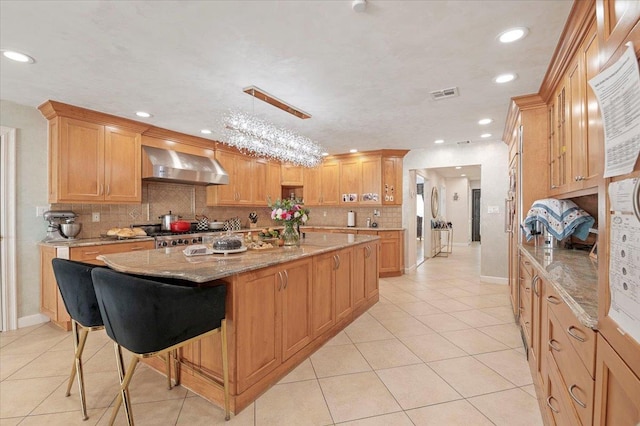 kitchen with light tile patterned floors, visible vents, wall chimney exhaust hood, a center island, and light stone countertops