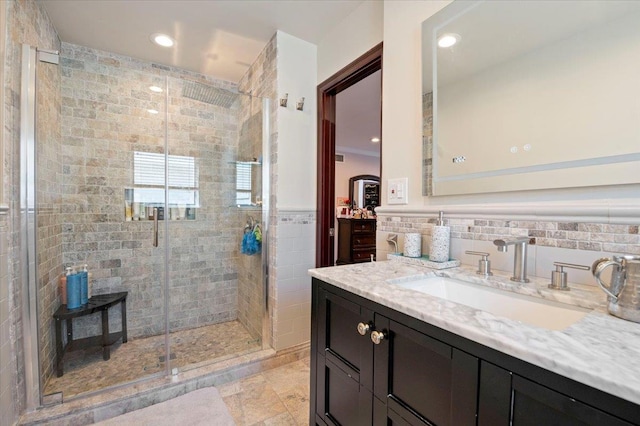 bathroom with tile walls, recessed lighting, wainscoting, a shower stall, and vanity