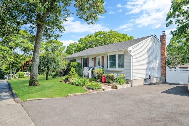 ranch-style home featuring driveway, a chimney, fence, and a front yard