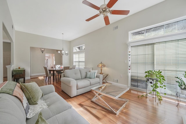 living room with light wood-style flooring, visible vents, baseboards, and ceiling fan with notable chandelier