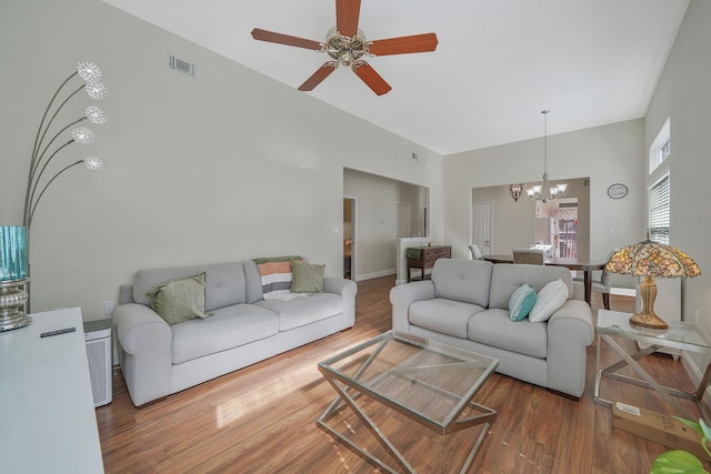 living room with a high ceiling, visible vents, wood finished floors, and ceiling fan with notable chandelier