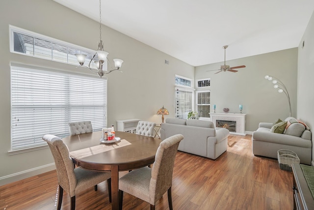 dining area with visible vents, baseboards, a glass covered fireplace, light wood-style floors, and ceiling fan with notable chandelier