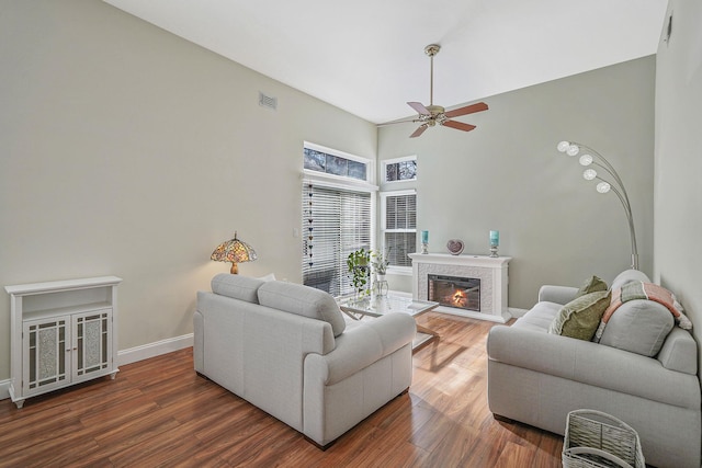 living room featuring wood finished floors, a ceiling fan, visible vents, baseboards, and a glass covered fireplace