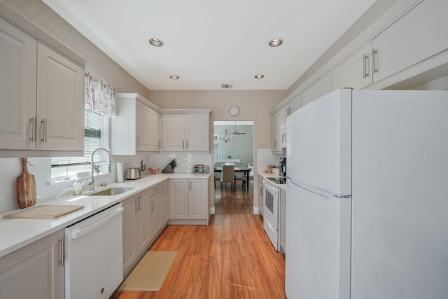 kitchen with white appliances, white cabinets, light countertops, light wood-type flooring, and a sink