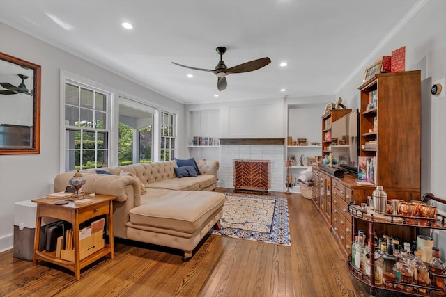 living room with recessed lighting, ornamental molding, a ceiling fan, a brick fireplace, and wood finished floors