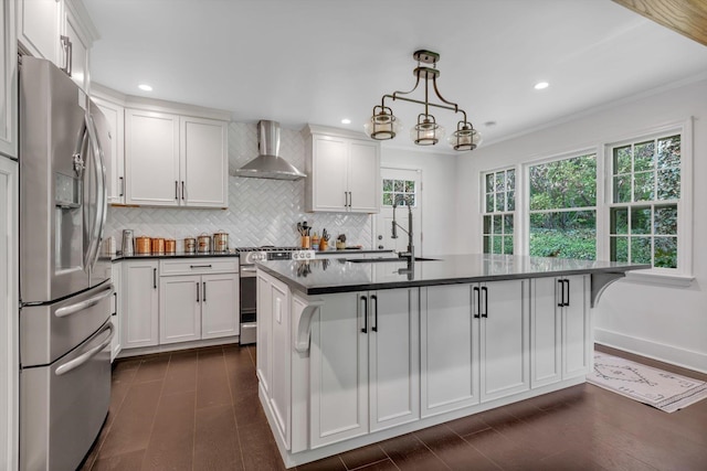 kitchen with dark countertops, stainless steel appliances, wall chimney range hood, white cabinetry, and a sink