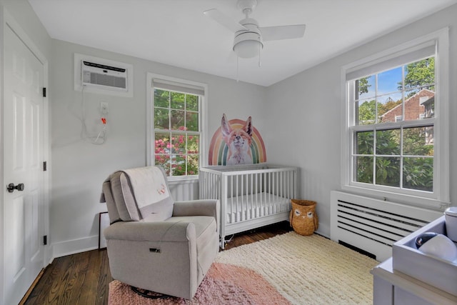 bedroom featuring a crib, radiator, dark wood-style floors, ceiling fan, and a wall mounted air conditioner