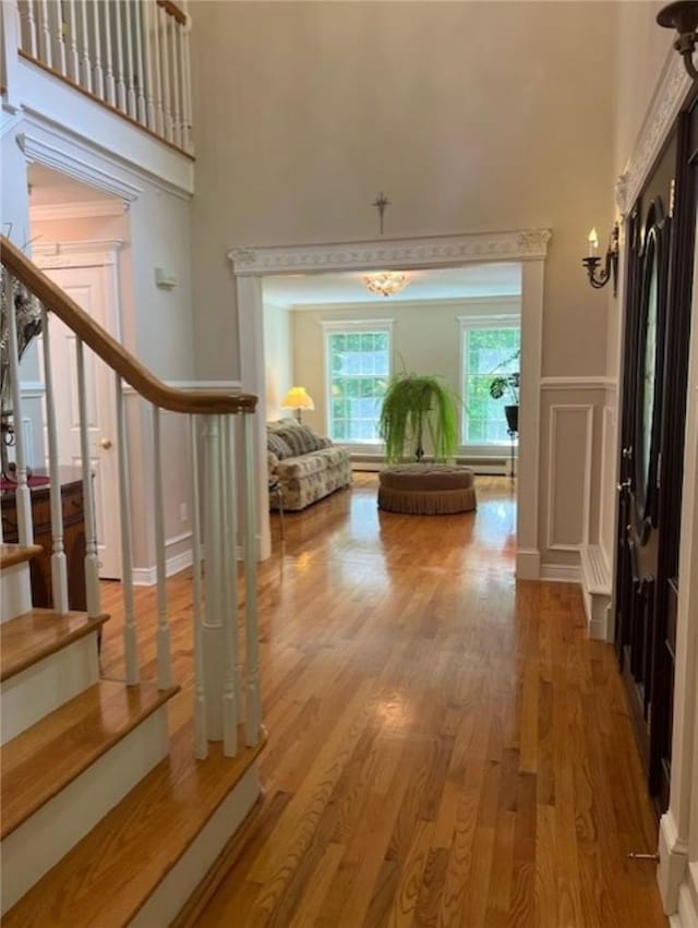 corridor with a high ceiling, stairway, a decorative wall, and wood finished floors