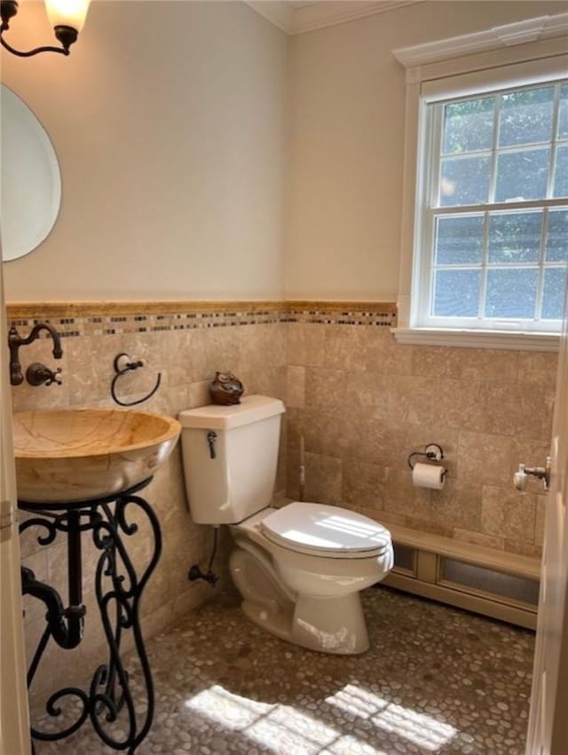 half bathroom featuring wainscoting, toilet, ornamental molding, a sink, and tile walls