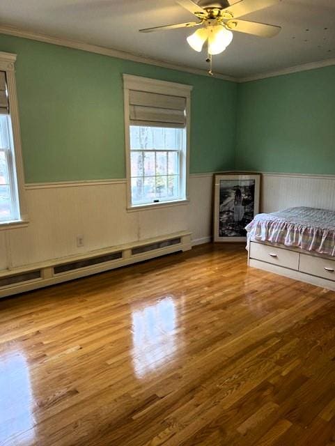 unfurnished bedroom featuring a wainscoted wall, multiple windows, baseboard heating, and wood finished floors