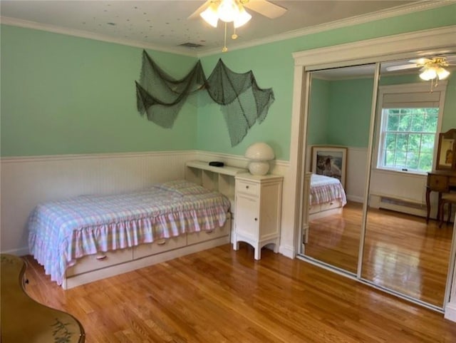 bedroom with a wainscoted wall, wood finished floors, and crown molding