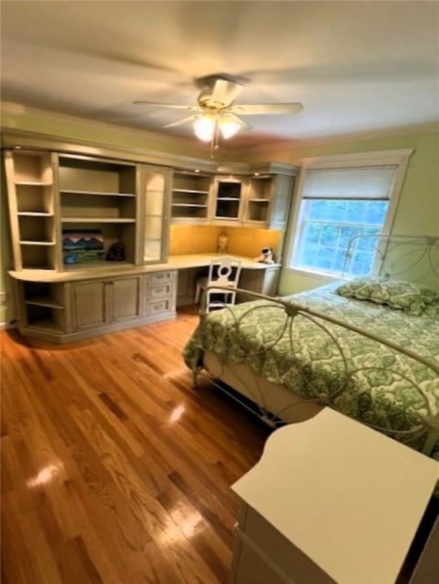 bedroom with ceiling fan, wood finished floors, and built in study area