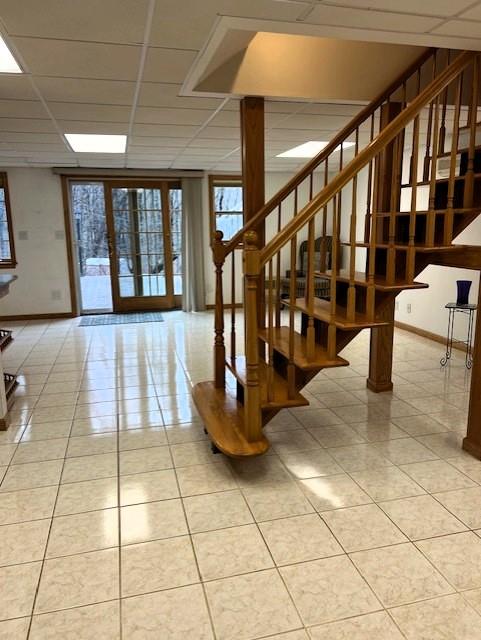 entryway with a paneled ceiling, light tile patterned floors, stairs, and baseboards