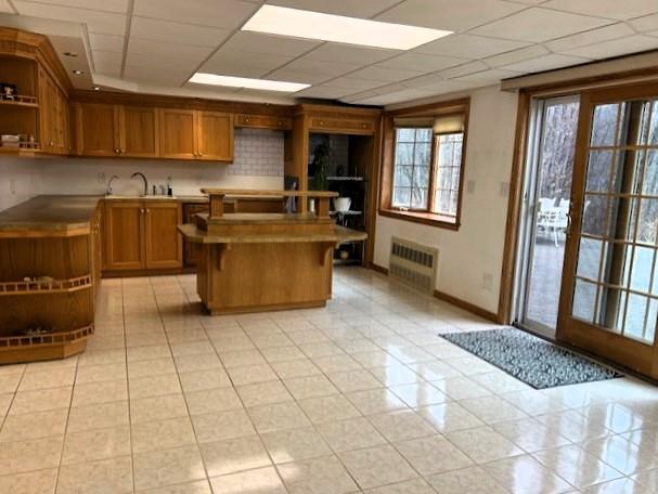 kitchen with a center island, light tile patterned floors, open shelves, radiator, and a drop ceiling