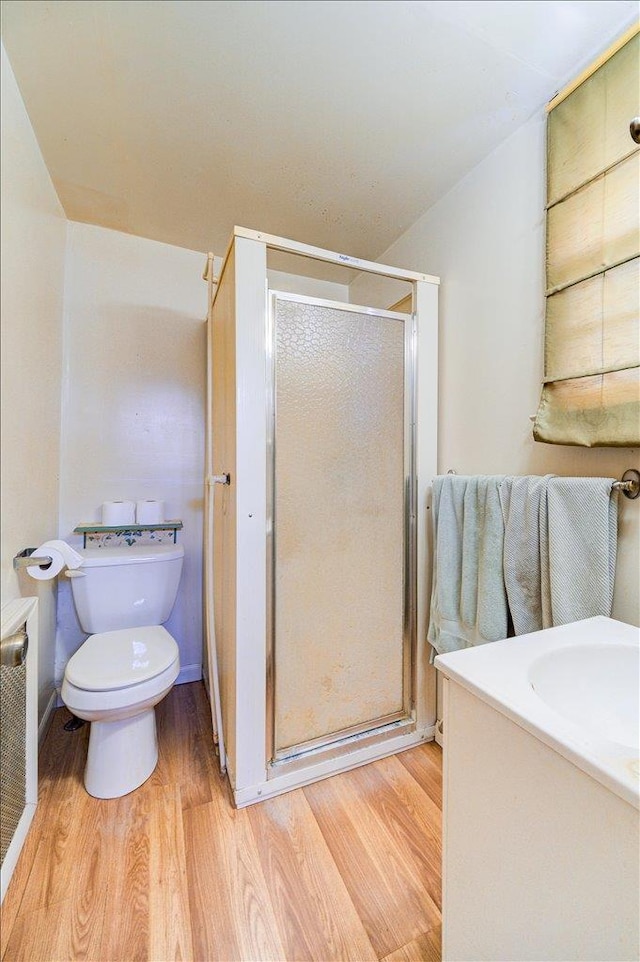 bathroom with toilet, a shower stall, wood finished floors, and vanity