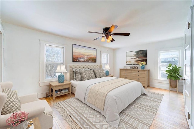 bedroom with light wood-type flooring, multiple windows, baseboards, and a ceiling fan