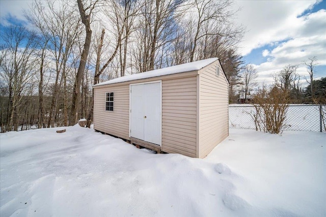 snow covered structure featuring an outbuilding, a storage unit, and fence