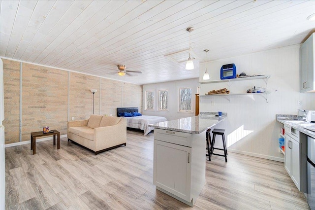 kitchen with light wood-style flooring, a breakfast bar area, a peninsula, light stone countertops, and pendant lighting