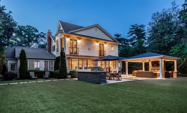 back of property featuring an outdoor kitchen, a gazebo, a lawn, a chimney, and a patio area