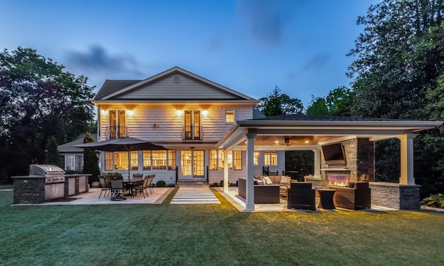 back of property featuring a patio area, a yard, an outdoor kitchen, and an outdoor living space with a fireplace