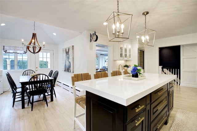 kitchen with hanging light fixtures, vaulted ceiling, light countertops, light wood-type flooring, and a chandelier