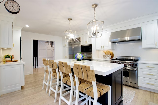 kitchen featuring built in appliances, light wood-style flooring, light countertops, wall chimney range hood, and a kitchen bar