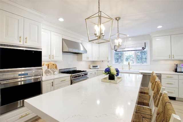 kitchen featuring a center island, appliances with stainless steel finishes, white cabinets, a sink, and wall chimney exhaust hood