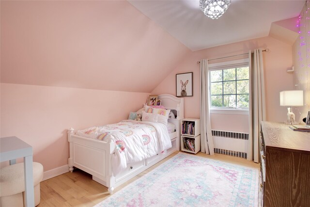 bedroom featuring light wood-type flooring, lofted ceiling, baseboards, and radiator heating unit