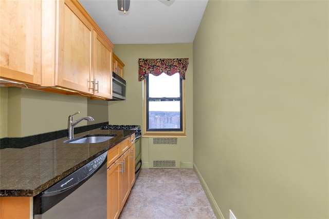 kitchen with stainless steel appliances, radiator, a sink, dark stone counters, and baseboards