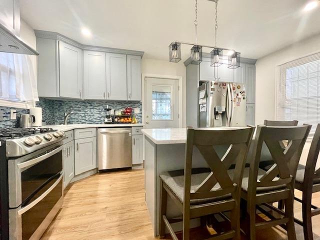 kitchen featuring gray cabinetry, light countertops, appliances with stainless steel finishes, decorative backsplash, and a kitchen bar