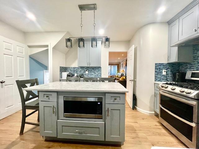 kitchen featuring appliances with stainless steel finishes, backsplash, light wood-style floors, and gray cabinetry