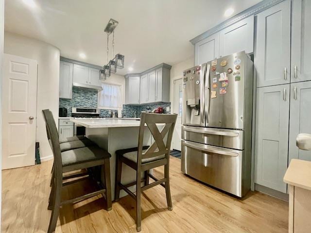 kitchen with light wood finished floors, a kitchen island, stainless steel appliances, light countertops, and a kitchen bar