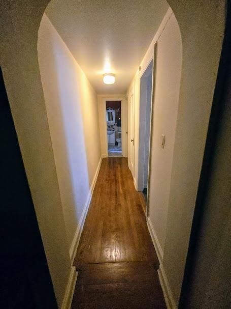 corridor with arched walkways, baseboards, and wood finished floors